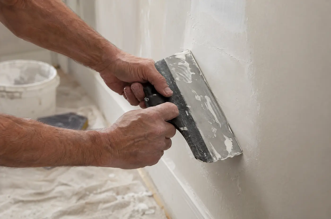 A drywall patch being smoothed with a wide knife on a living room wall